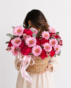 a woven basket filled with pink and red flowers, including daisies and carnations, with green foliage and a pink ribbon, Edmonton flowers 