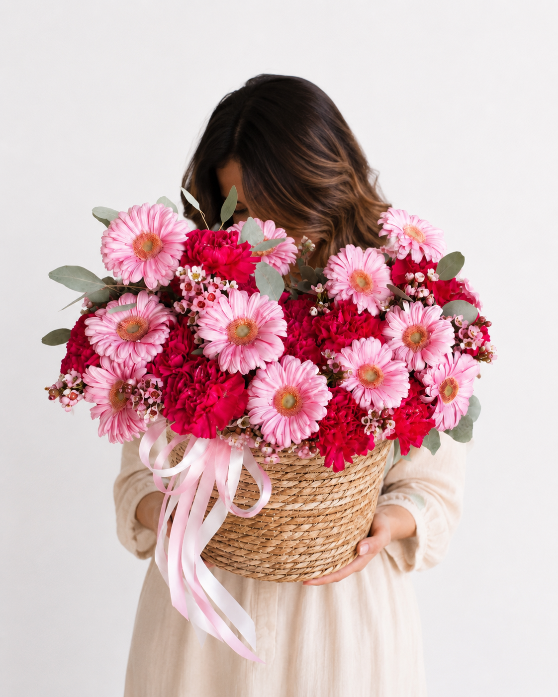 a woven basket filled with pink and red flowers, including daisies and carnations, with green foliage and a pink ribbon, Edmonton flowers 